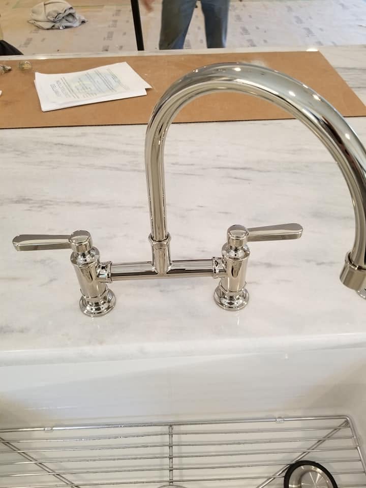 Chrome bridge faucet installed on a marble kitchen countertop